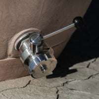 Primer plano de la válvula de salida triclampe de acero inoxidable con palanca de control y conexión Mâcon.